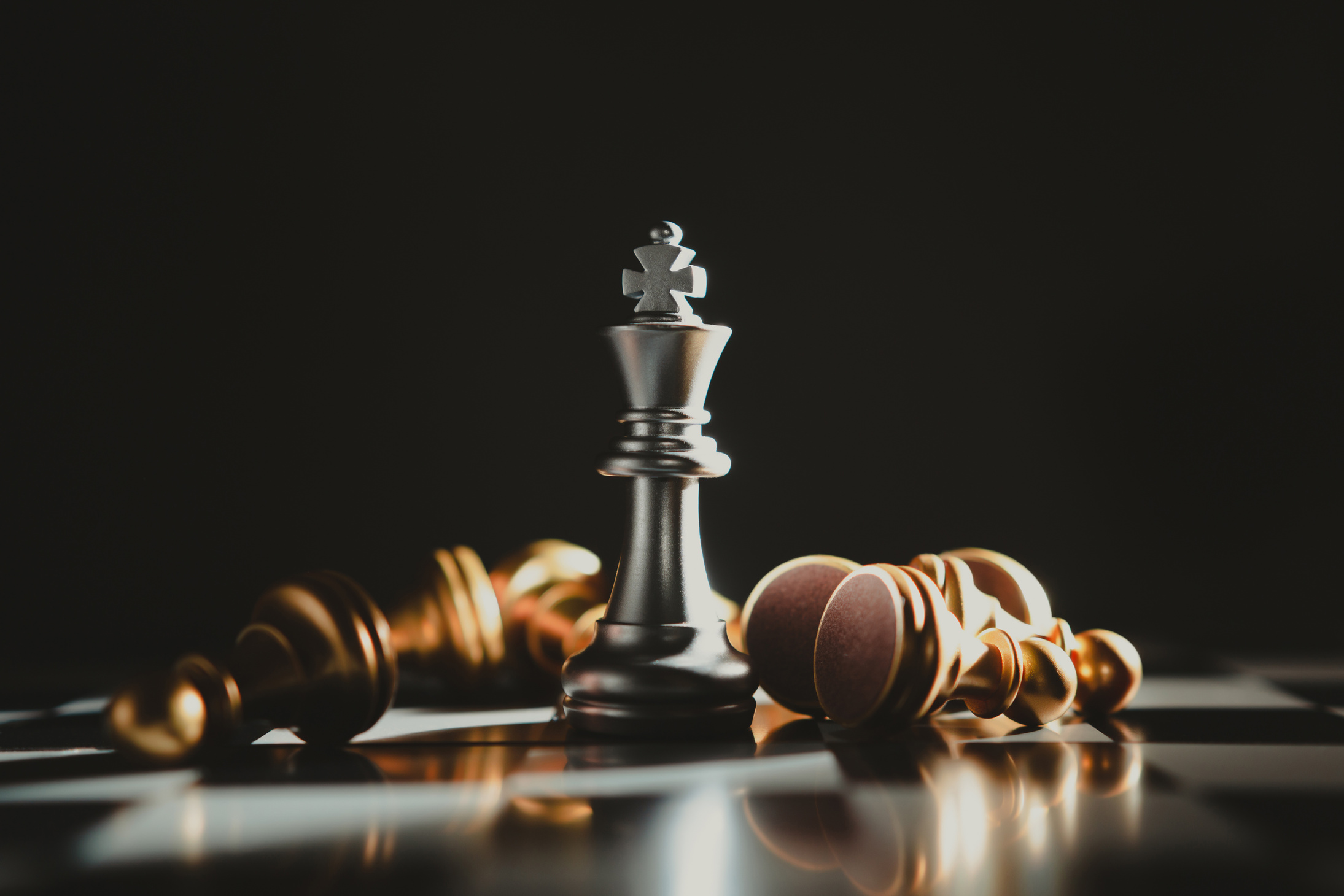 Silver chess king surrounded by gold chess pieces.